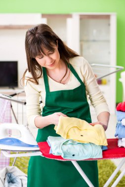 Evde giysileri ütüleyen genç bir kadın.