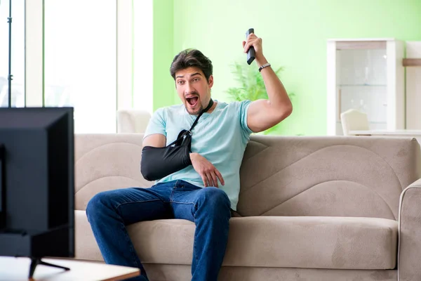 Arm injured man sitting on the sofa watching tv — Stock Photo, Image