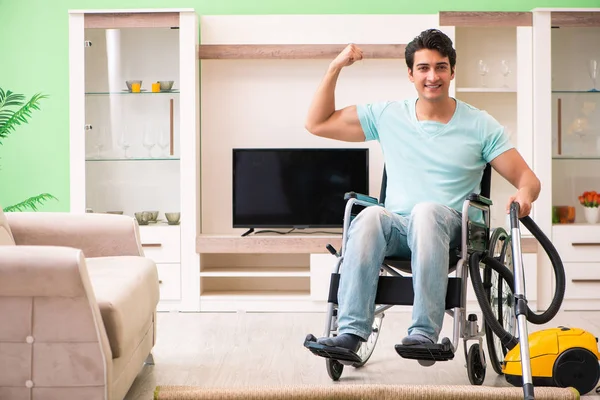 Tekerlekli sandalyedeki engelli adam elektrikli süpürge evi. — Stok fotoğraf