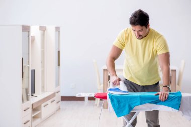 Yakışıklı koca evde kıyafet ütülüyor.