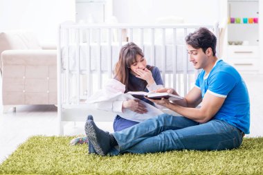 Yeni doğmuş bebekleriyle halıda oturan genç ebeveynler. 