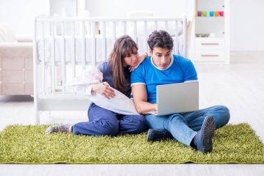 Yeni doğmuş bebekleriyle halıda oturan genç ebeveynler. 