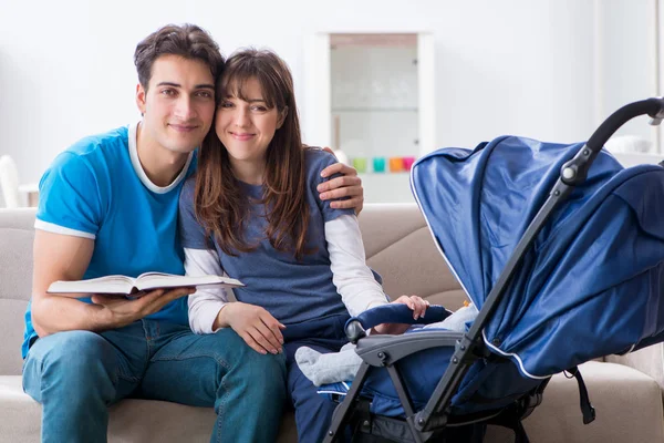 Young parents with their newborn baby in baby pram sitting on the sofa — Stock Photo, Image