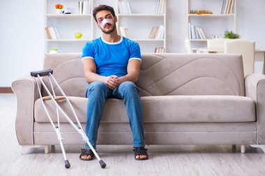 Koltuk değnekli yaralı bir adam evde iyileşiyor. 