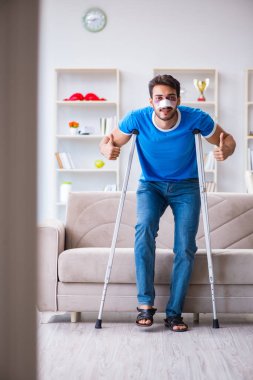 Koltuk değnekli yaralı bir adam evde iyileşiyor. 