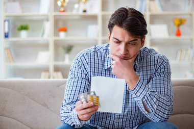 Kanepede ilaç ve reçeteyle oturan genç adam.