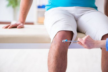 Doktor çekiçle sinir reflekslerini kontrol ediyor