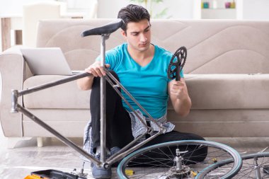 Evde bisiklet tamir eden genç bir adam.