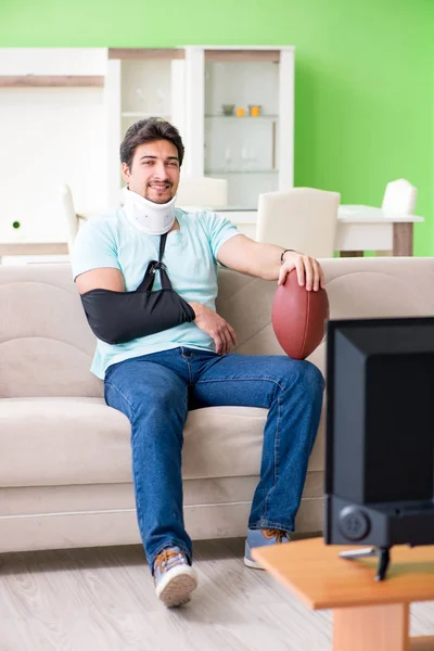 Uomo con lesioni al collo e al braccio guardando il calcio americano in tv — Foto Stock