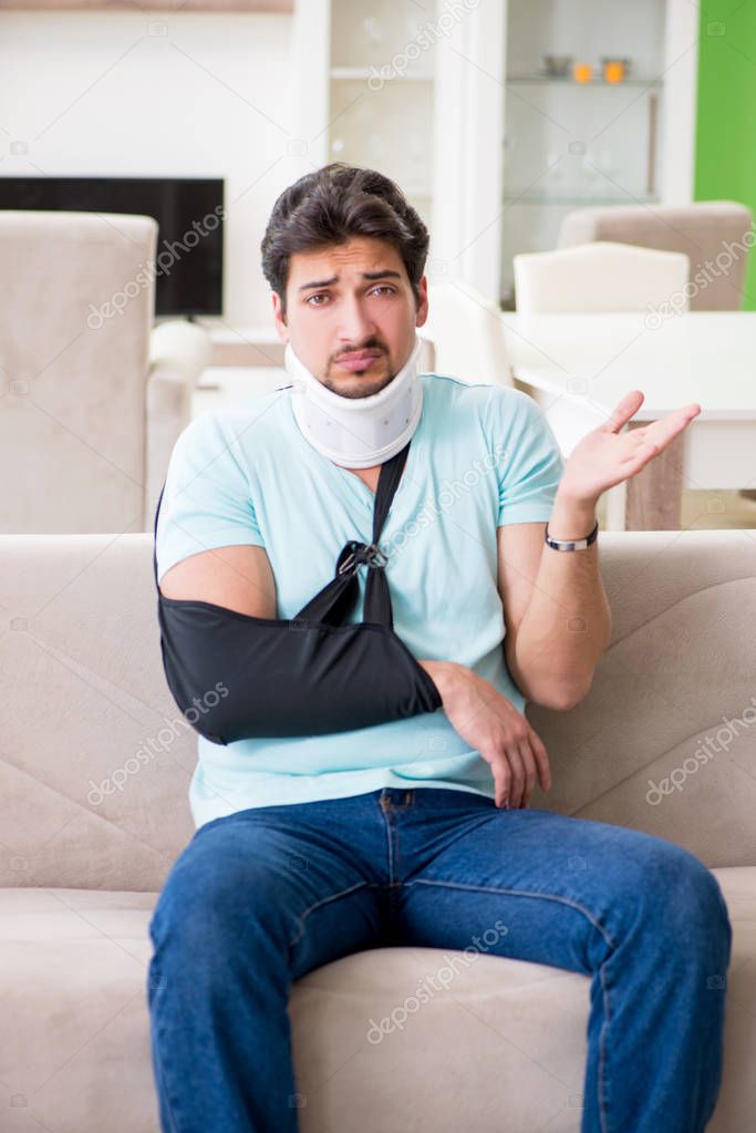 Young student man with neck and hand injury sitting on the sofa