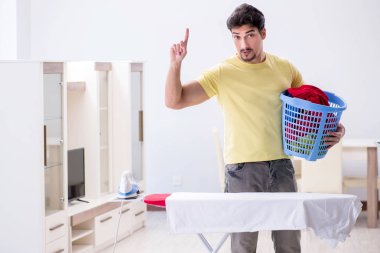 Yakışıklı koca evde kıyafet ütülüyor.