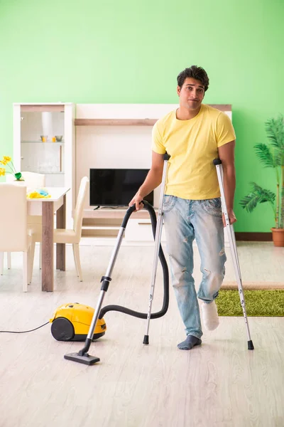 Injured man on crutches vacuum cleaning house