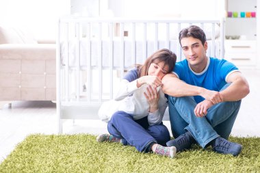 Yeni doğmuş bebekleriyle halıda oturan genç ebeveynler. 