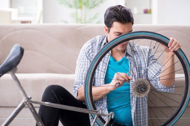 Evde bisiklet tamir eden genç bir adam.