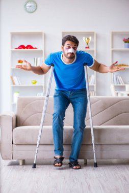 Koltuk değnekli yaralı bir adam evde iyileşiyor. 