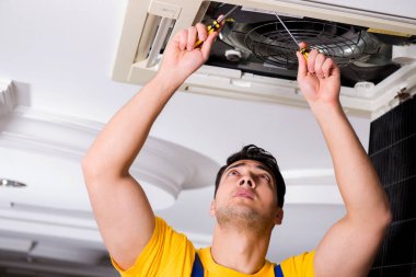 Tamirci tavan havalandırma ünitesini tamir ediyor.