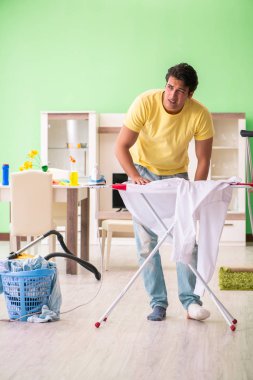 Bacağı yaralı adam evde ütü yapıyor.