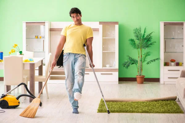 Injured man on crutches cleaning house