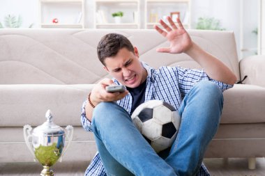 Evde futbol izleyen genç bir öğrenci.