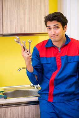 Tesisatçı mutfakta musluğu tamir ediyor.