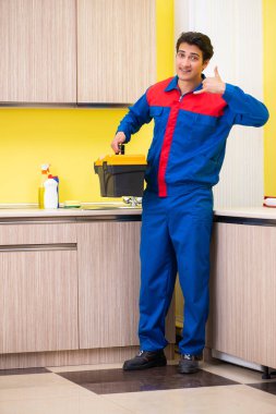 Tesisatçı mutfakta musluğu tamir ediyor.