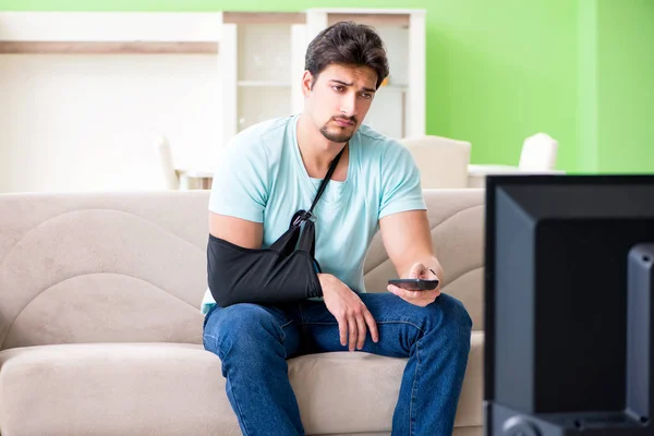 Brazo herido hombre sentado en el sofá viendo la televisión — Foto de Stock