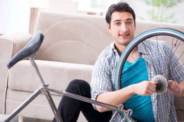 Evde bisiklet tamir eden genç bir adam.