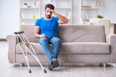 Koltuk değnekli yaralı bir adam evde iyileşiyor. 