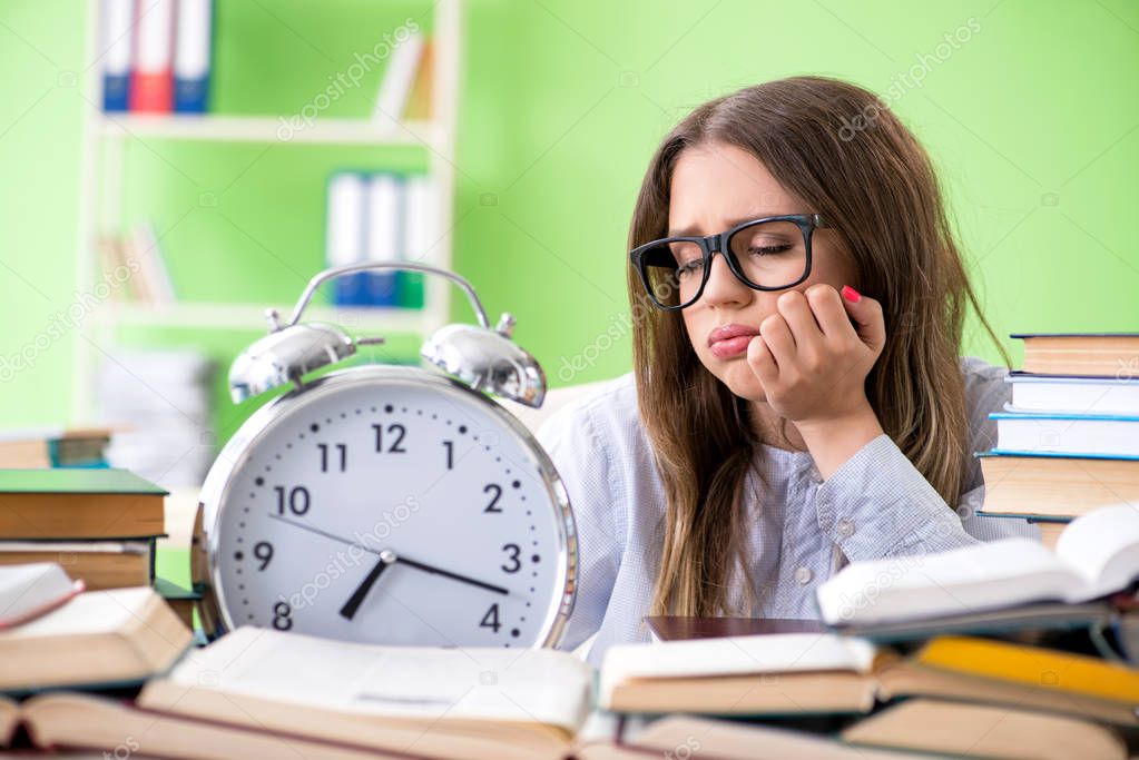 Young female student preparing for exams with many books in time