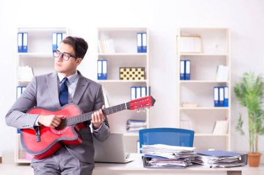 Genç yakışıklı işadamı ofiste gitar çalıyor. 