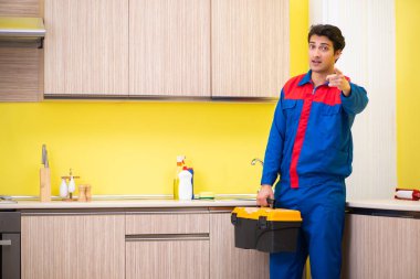 Tesisatçı mutfakta musluğu tamir ediyor.