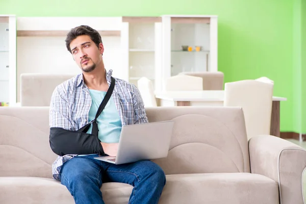 Mladý student muž s poraněním ruky sedí na pohovce — Stock fotografie