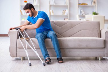 Koltuk değnekli yaralı bir adam evde iyileşiyor. 