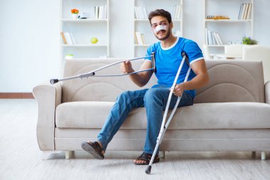 Koltuk değnekli yaralı bir adam evde iyileşiyor. 