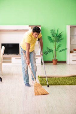 Koltuk değnekli yaralı bir adam evi temizliyor.