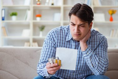 Kanepede ilaç ve reçeteyle oturan genç adam.