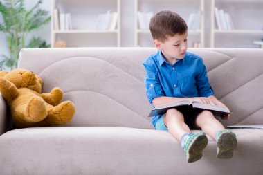 Evde kitap okuyan küçük bir çocuk.