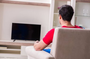 Genç adam evde televizyon izliyor.