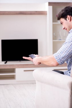 Genç adam evde televizyon izliyor.