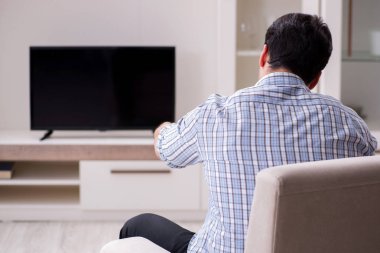 Genç adam evde televizyon izliyor.