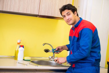 Tesisatçı mutfakta musluğu tamir ediyor.