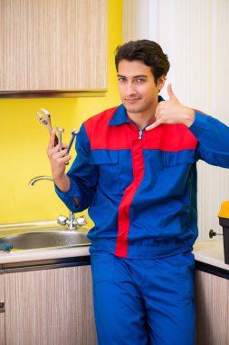 Tesisatçı mutfakta musluğu tamir ediyor.