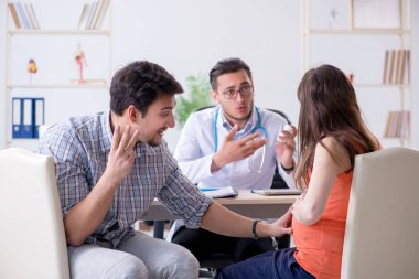 Hamile kadın kocasıyla klinikteki doktoru ziyaret ediyor.