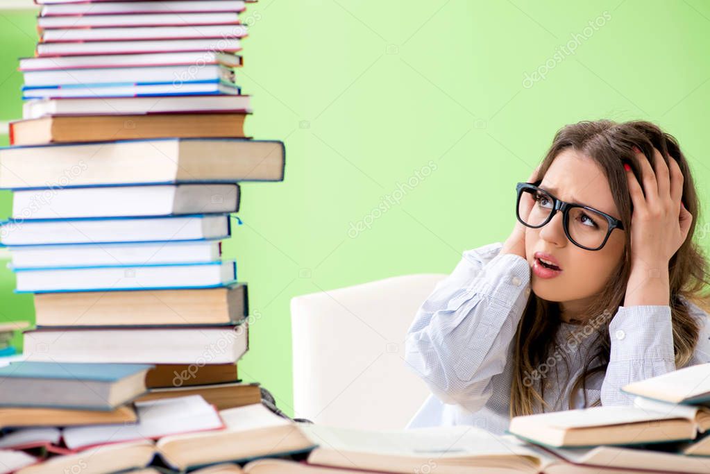 Young female student preparing for exams with many books 