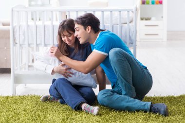 Yeni doğmuş bebekleriyle halıda oturan genç ebeveynler. 