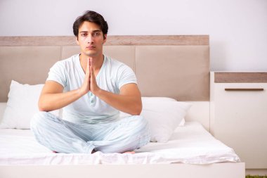 Genç adam yatakta yoga yapıyor.