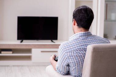 Genç adam evde televizyon izliyor.