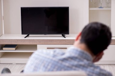 Genç adam evde televizyon izliyor.