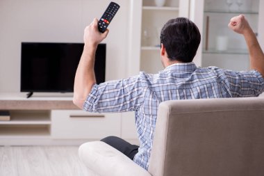 Genç adam evde televizyon izliyor.