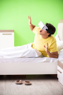 Yatak odasında sanal gözlüklü genç adam. 